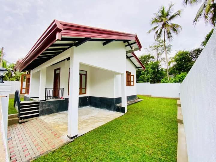a small house with a green lawn in front of it at Himeth's Residence in Weliweriya