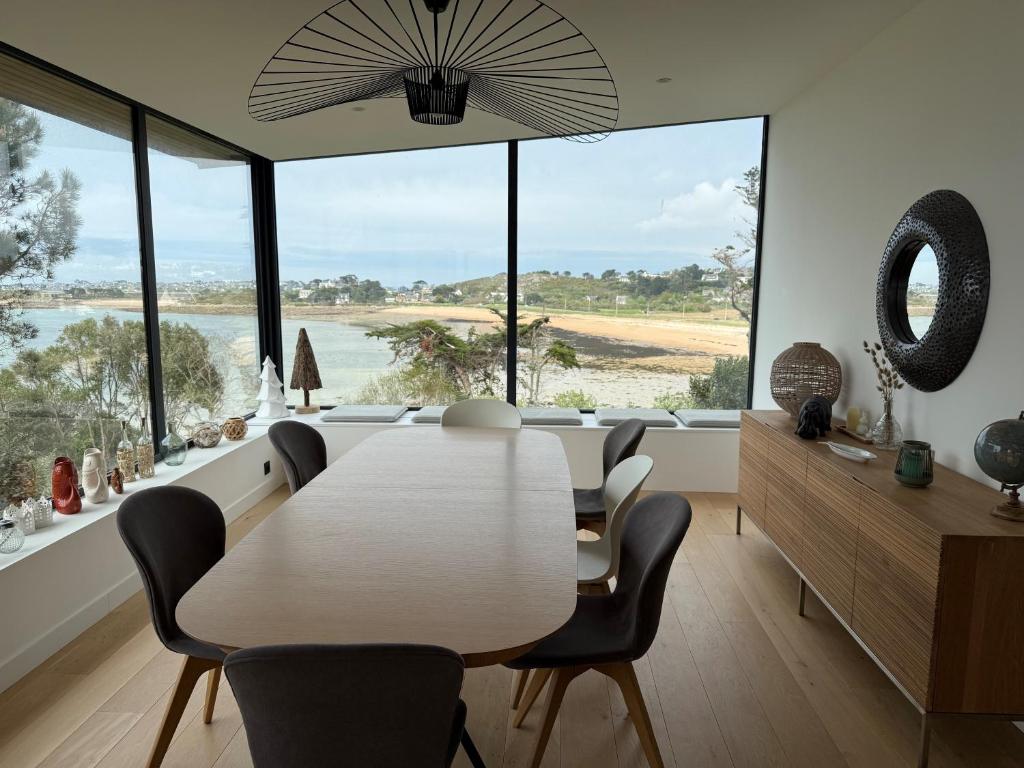 a dining room with a table and chairs and large windows at Maison les pieds dans l'eau in Trébeurden