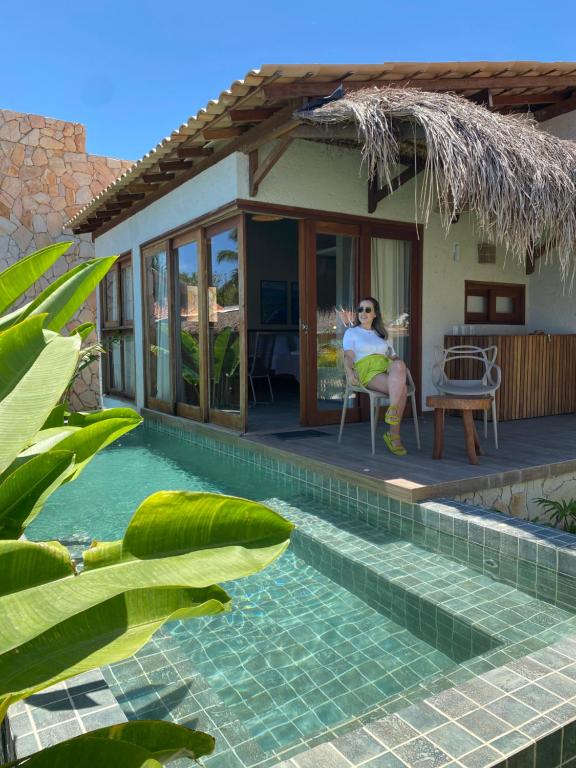 a woman sitting on the porch of a house with a pool at Villa Mar Milagres - bangalôs de luxo em São Miguel dos Milagres, Alagoas in São Miguel dos Milagres