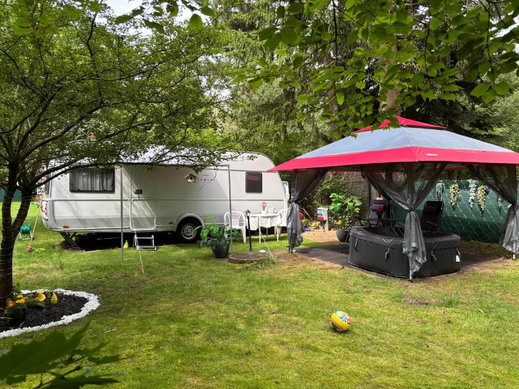 a tent in a yard with a caravan and a red umbrella at Lazy Days Caravan in Berlin