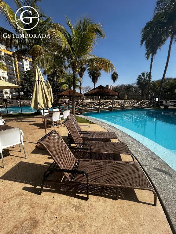 a group of chairs and umbrellas next to a swimming pool at Hotel suits Le jardin in Caldas Novas