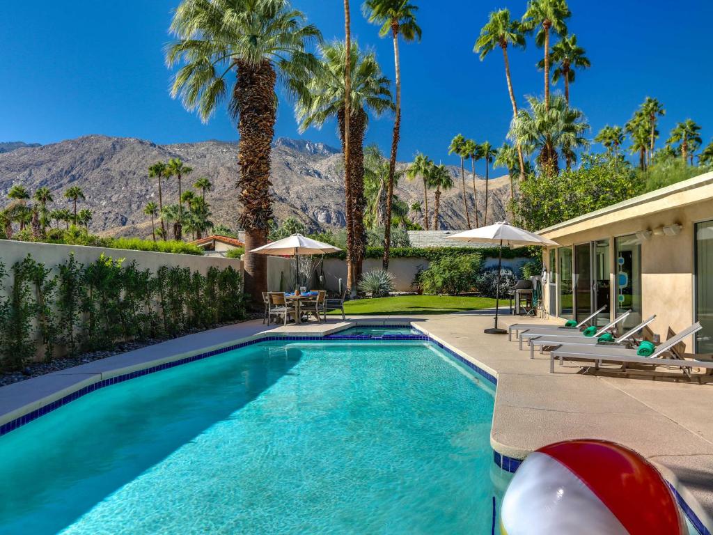 a swimming pool with palm trees and a house at Movie Colony Palms by ACME House Company in Palm Springs
