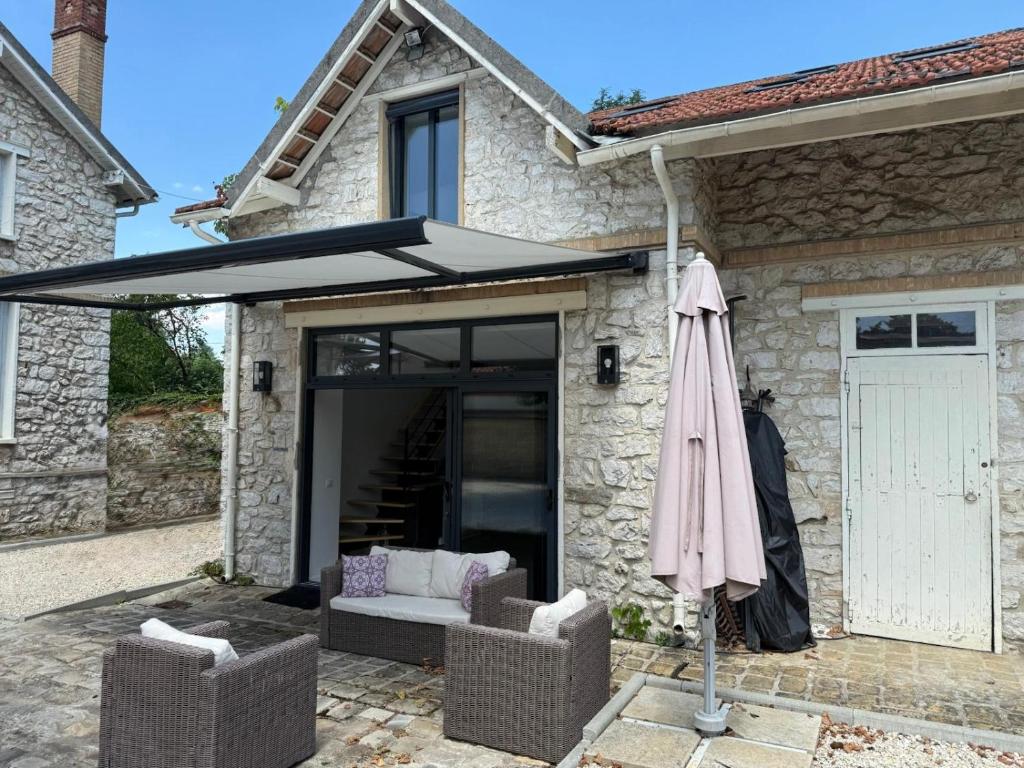 a patio with an umbrella and two chairs and a couch at Dépendance près de Fontainebleau in Vulaines-sur-Seine
