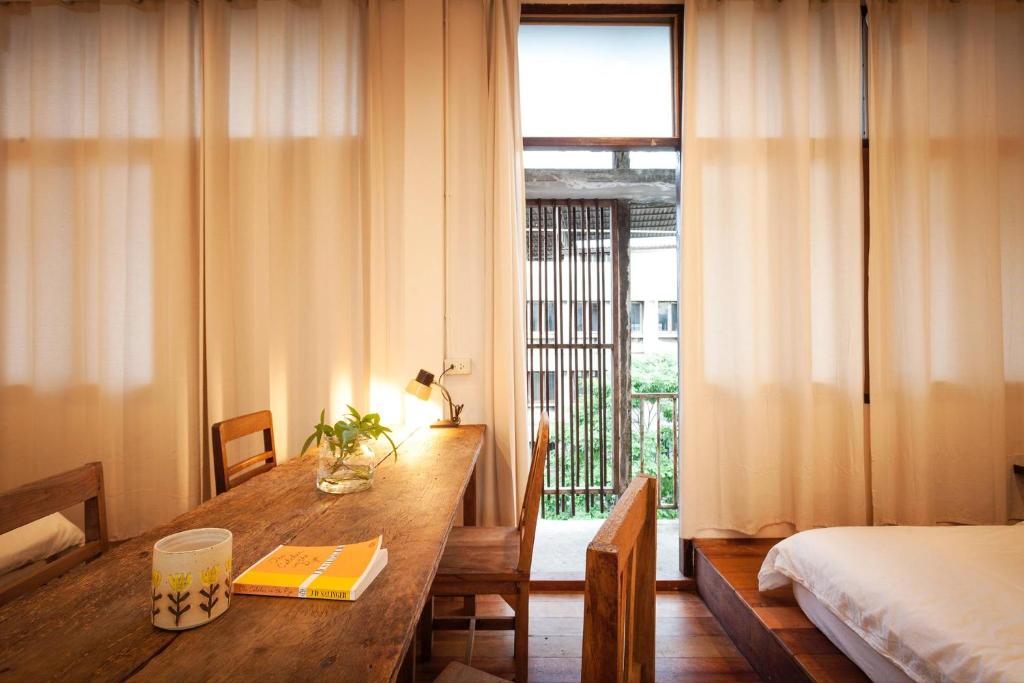 A bedroom corner with a long wooden worktable beside a curtained window.