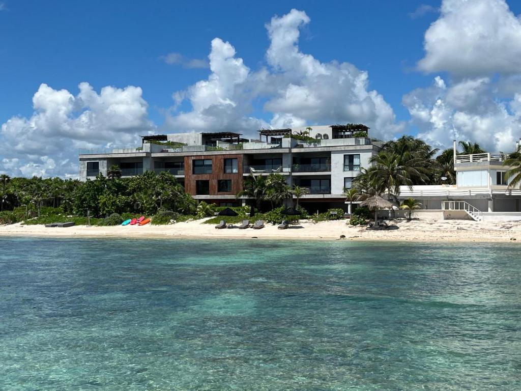 a building on the beach next to the water at Beachfront 3BR Condo with Private Rooftop and lounge pool, Tankah Bay in Tulum
