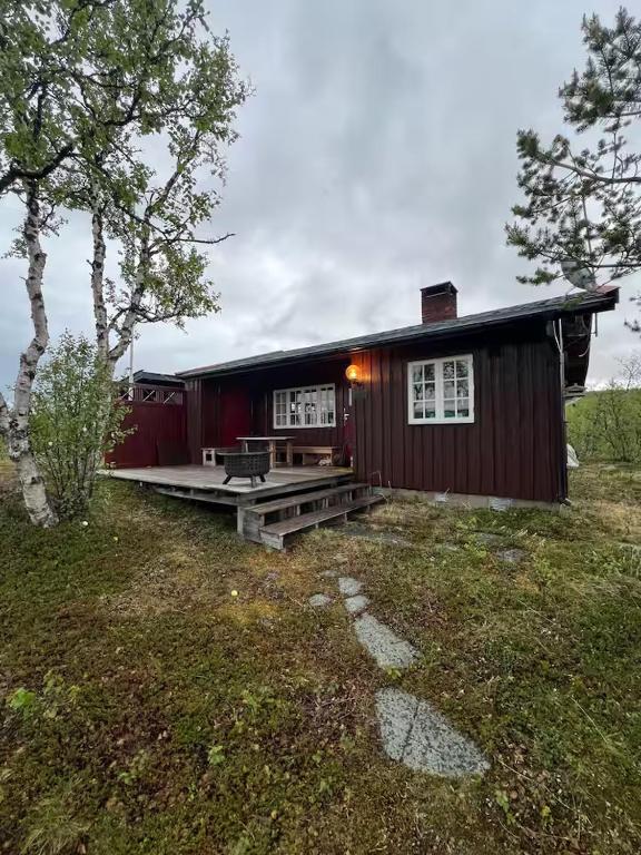 a small red house with a porch in a field at Cabin in Silisjávri in Skillemo