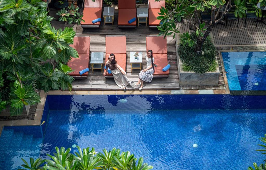 two women sitting on chairs next to a swimming pool at Amber Angkor Villa Hotel & Spa in Siem Reap