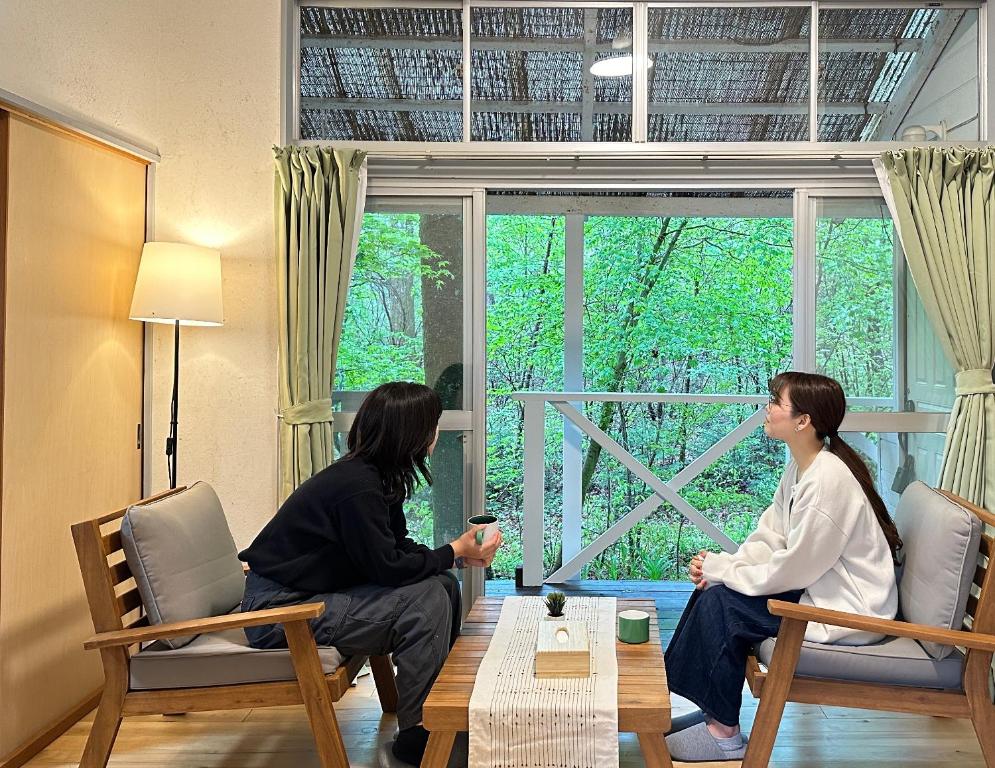 two women sitting around a table in a room with a window at Summer Cool Forest Cottage-北軽井沢 夏涼の森コテージ- in Tsumagoi