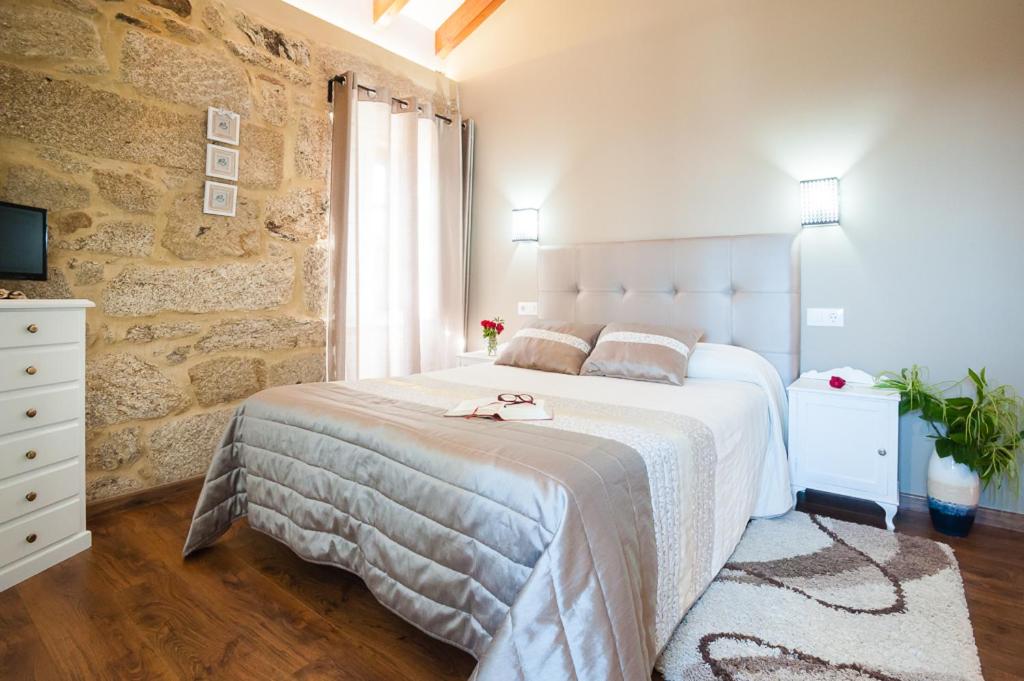 Un dormitorio con una gran cama blanca y una pared de piedra. en A Cantaruxa Maruxa Turismo Rural, en Mondariz