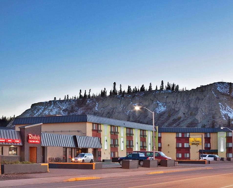 a building with a mountain in the background with cars parked at Quality Inn &amp; Suites in Whitehorse
