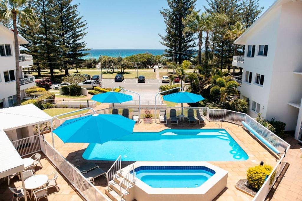 een bovenaanzicht van een zwembad met blauwe parasols bij Le Beach Apartments in Gold Coast