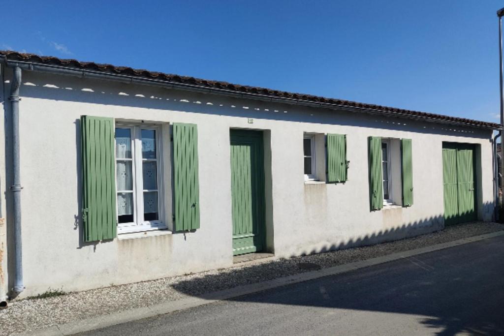 a white building with green shutters on a street at House ideal for families 10 min from the beaches in Le Bois-Plage-en-Ré