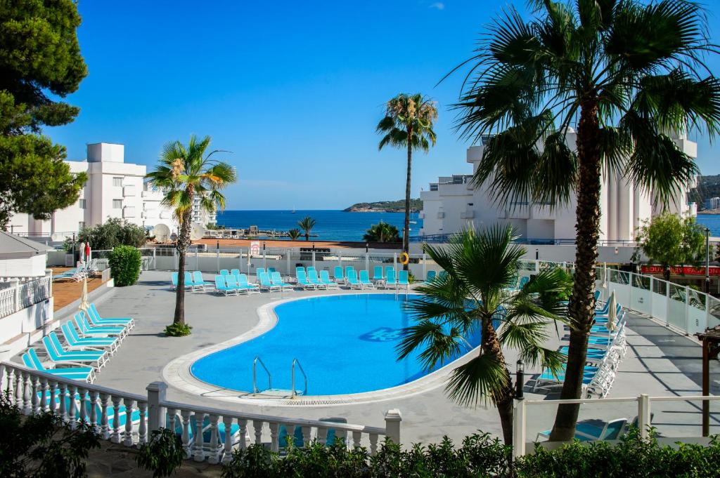 a pool with chairs and palm trees and the ocean at Apartamentos Vibra Riviera in San Antonio Bay