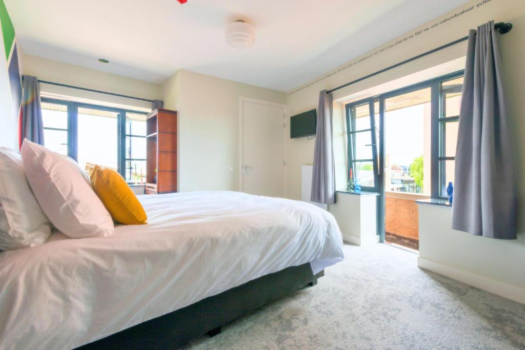 a bedroom with a bed with white sheets and windows at New Apart-hotel Near 013 Poppodium With Fast Wifi in Tilburg