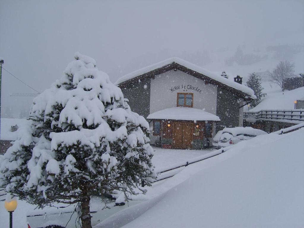 a snow covered house with a tree in front of it at Hotel Le Clocher in Champoluc