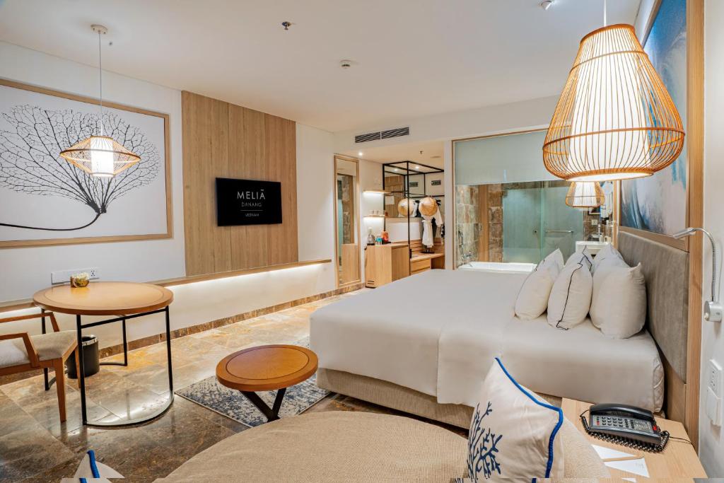 A polished king room with a large bed, lounge seating and a visible glass bathroom area.
