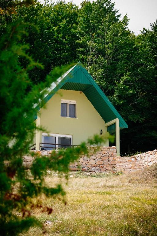 a house with a green roof and a stone wall at Forest Panorama Cabin Brezna in Pluzine
