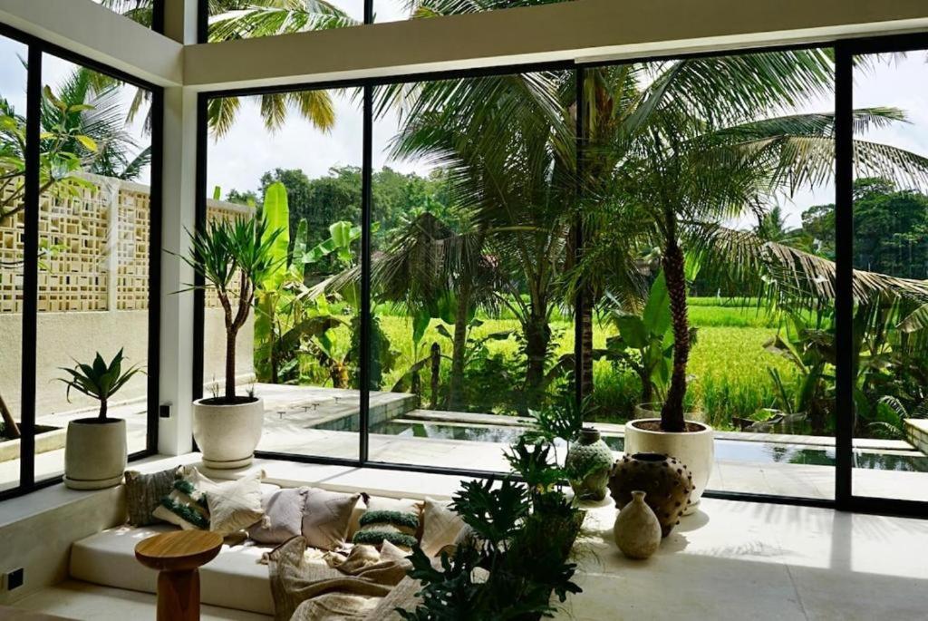 a living room with palm trees and a large window at Ubud Dzen Villa 8 in Ubud