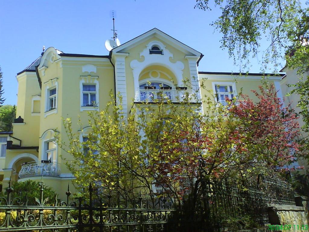 ein gelbes Haus mit einem Zaun davor in der Unterkunft Villa Sonnenstrahl in Marienbad
