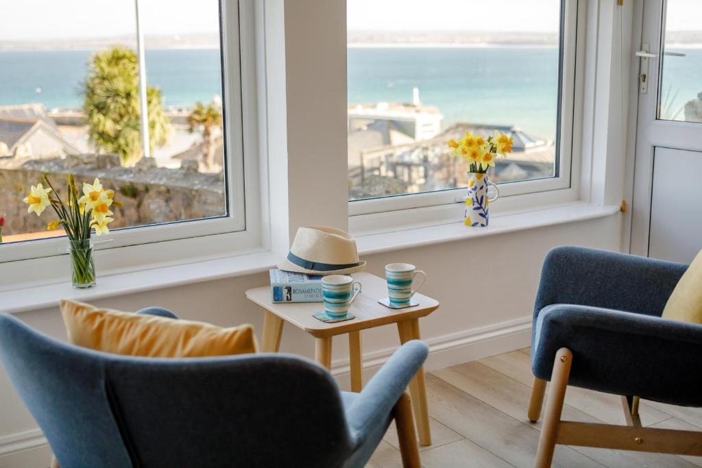 a living room with two chairs and a table and windows at 1 Seabirds House in St Ives
