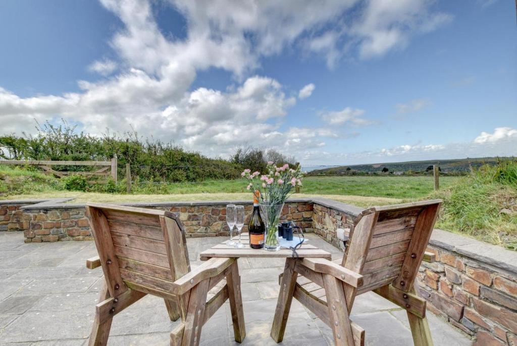 einen Tisch mit einer Flasche Wein und Blumen auf einer Terrasse in der Unterkunft Honeysuckle Cottage Welcombe in Welcombe