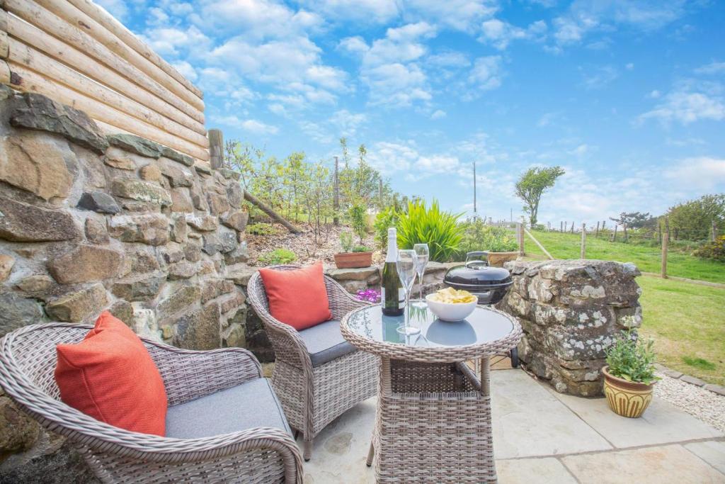 a patio with a table and chairs and a stone wall at Yr Hen Ysgubor in Bottwnog