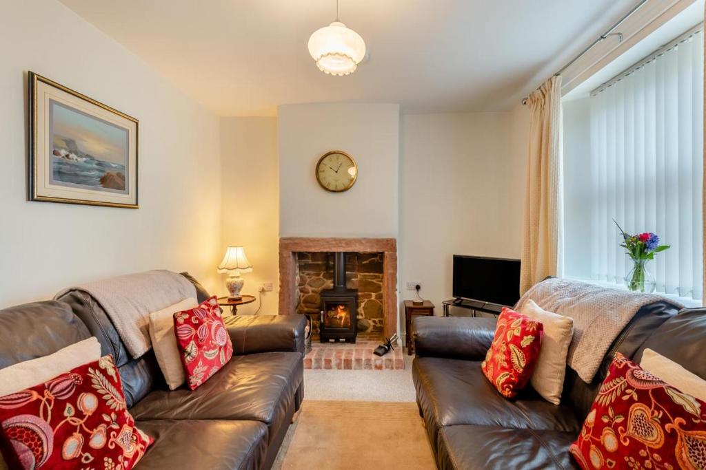 a living room with a leather couch and a fireplace at Iona Cottage - Allonby in Allonby