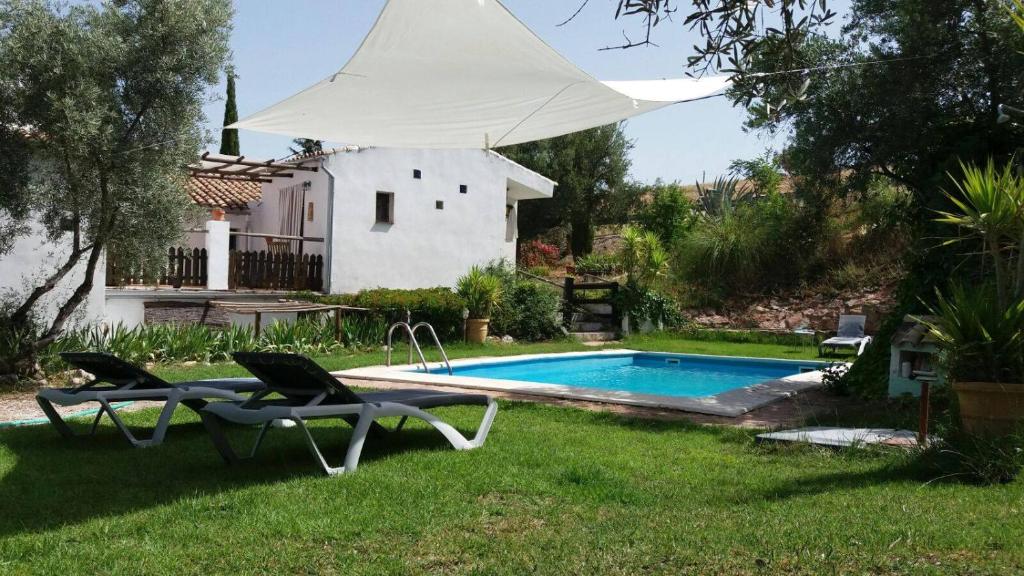 une piscine avec deux chaises et un parasol blanc dans l'établissement Posada Niña Margarita, à Priego de Córdoba
