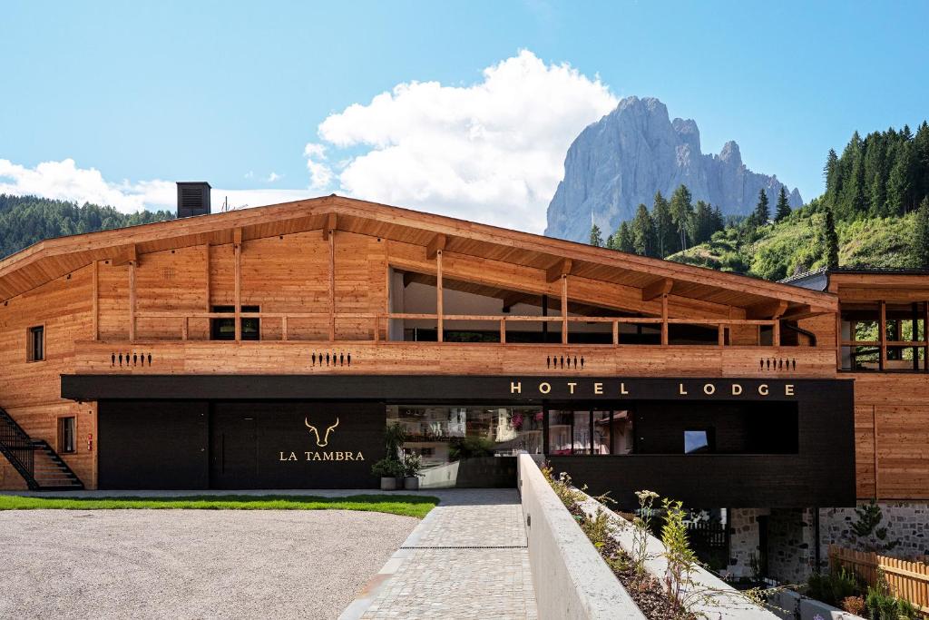 a wooden hotel building with mountains in the background at La Tambra - Hotel Lodge in Santa Cristina in Val Gardena