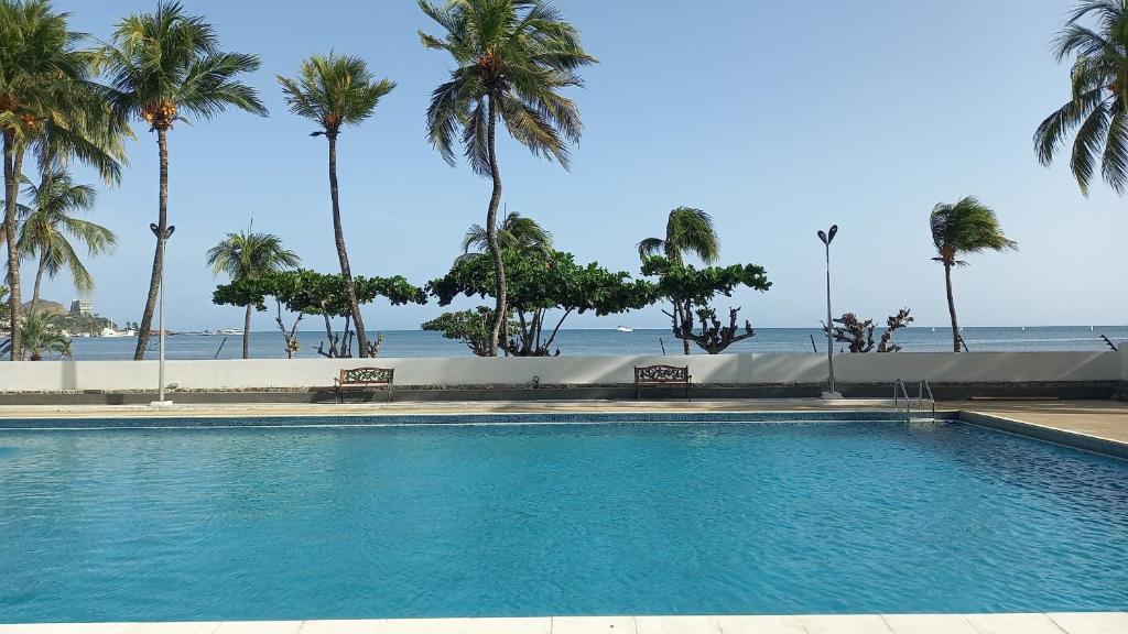 a swimming pool next to the beach with palm trees at Mar & Relax, apartamento en primera linea de playa in Porlamar