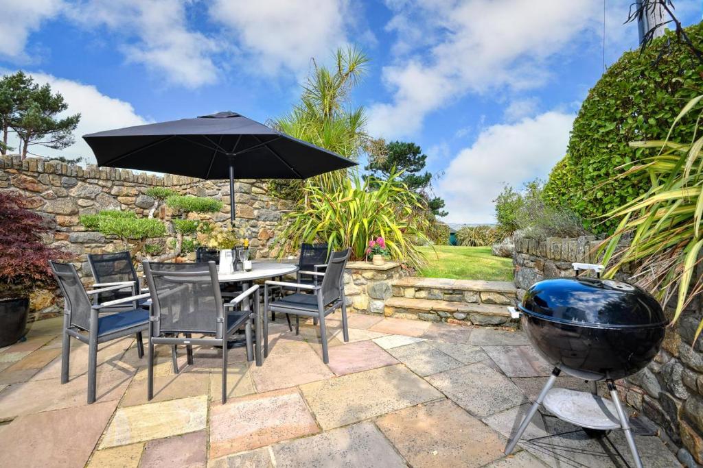 a patio with a table with an umbrella and a grill at Pengarth Cottage in Abersoch
