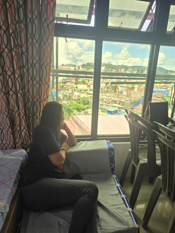 una mujer sentada en una cama mirando por la ventana en Bel's Cozy Suites at Lavernie, en Baguio