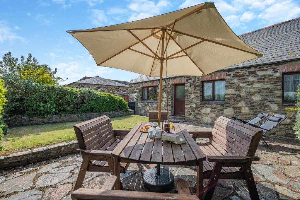 a wooden table with an umbrella on a patio at Mallard Cottage - Padstow in St Merryn