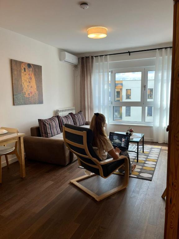 a woman sitting in a chair in a living room at Fantasia Apartment - Tesla palace in Kragujevac