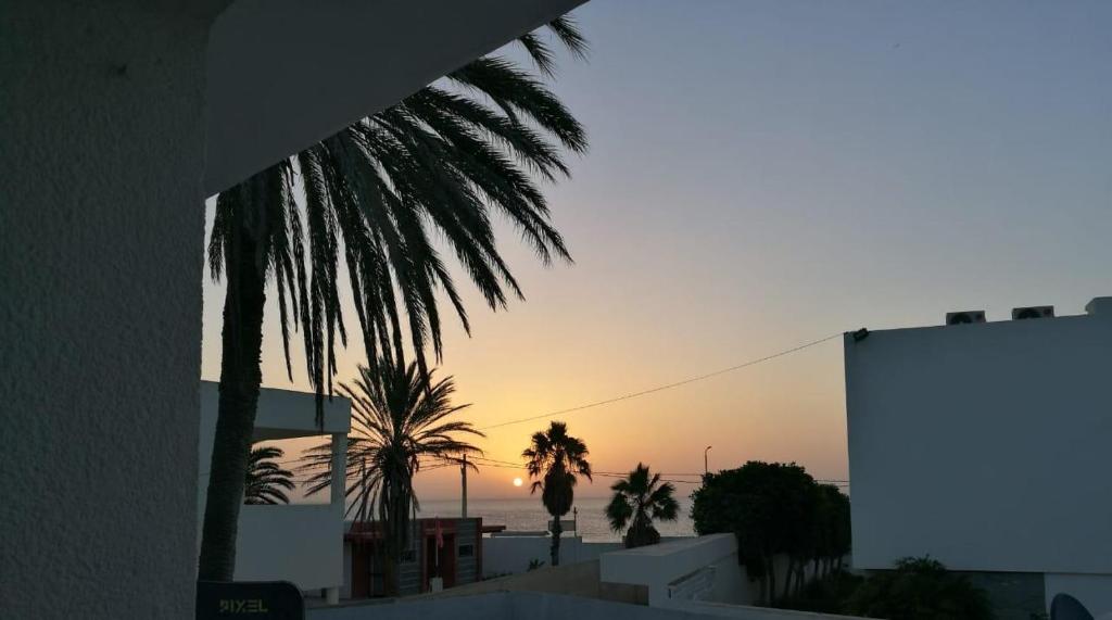 a view of a sunset from a building with palm trees at Évasion côtière à la Corniche - Villa sur la mer in Banzart