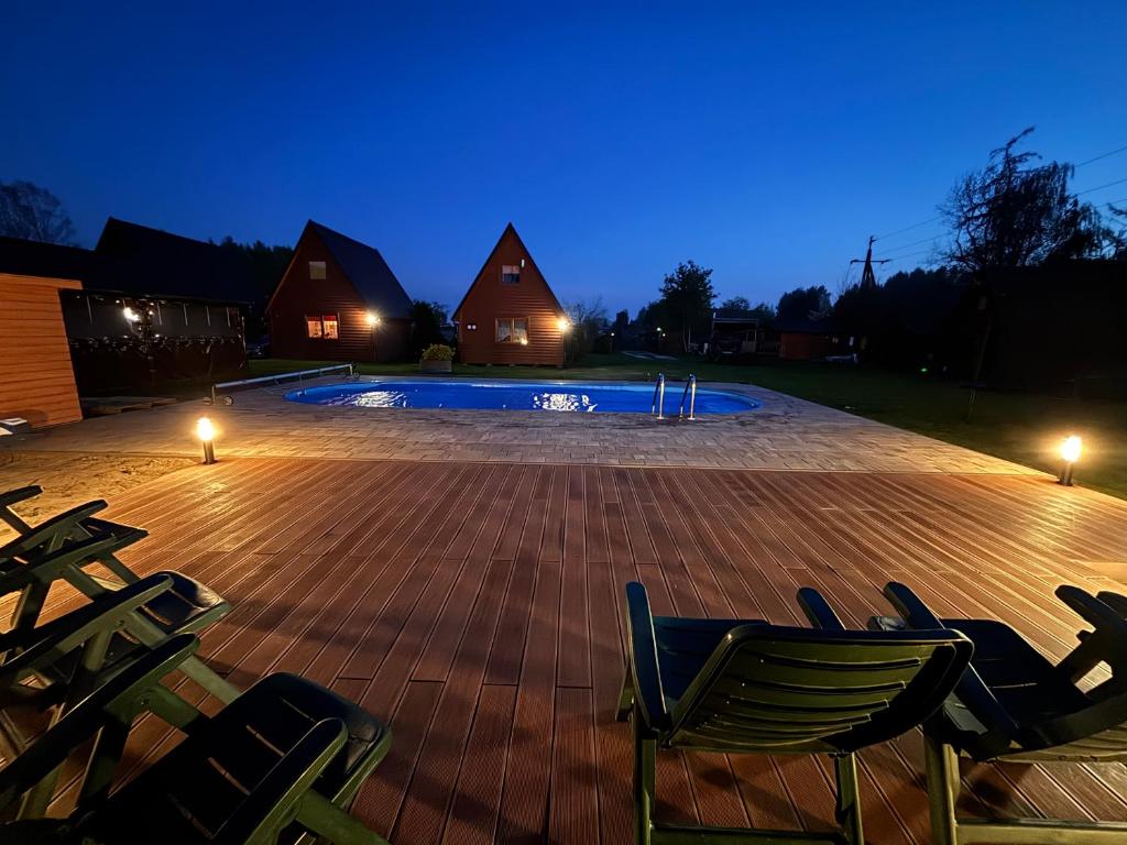 a deck with chairs and a swimming pool at night at Domki KANZAS in Sławno
