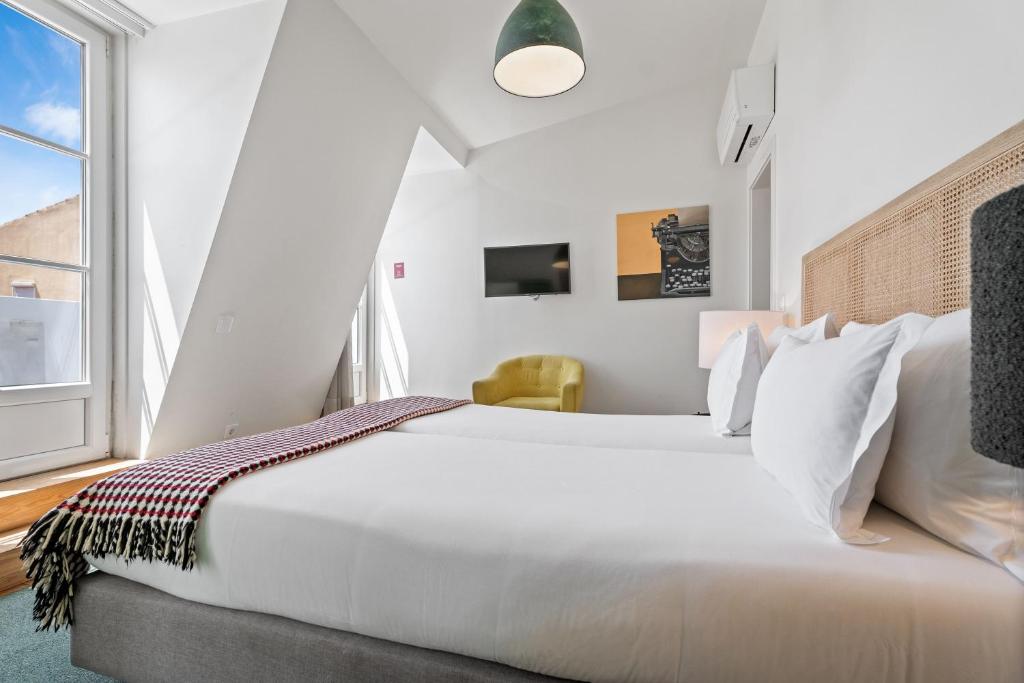 A bright guest room with a large bed, sloped ceiling, window, TV, and small armchair.