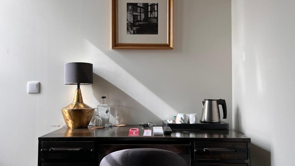 A compact desk with kettle, cups, water and a decorative lamp in a hotel room.