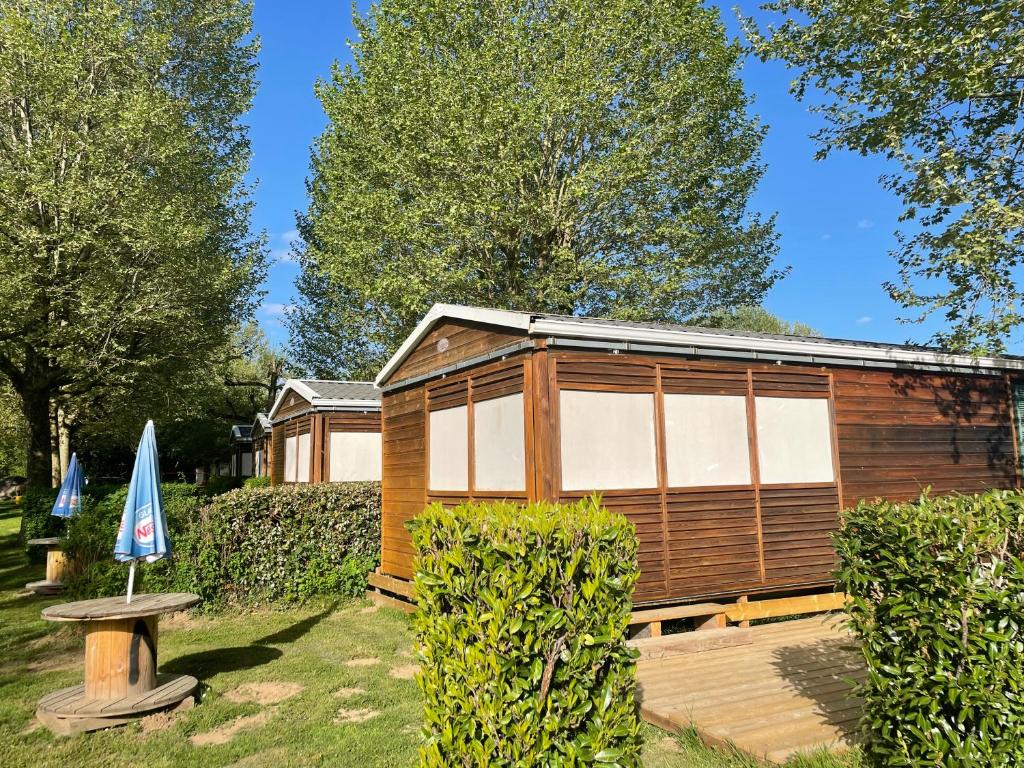 una cabina di legno in un cortile con una panchina e un ombrellone di Mobil-home 2 chambres côté rivière a Ébreuil