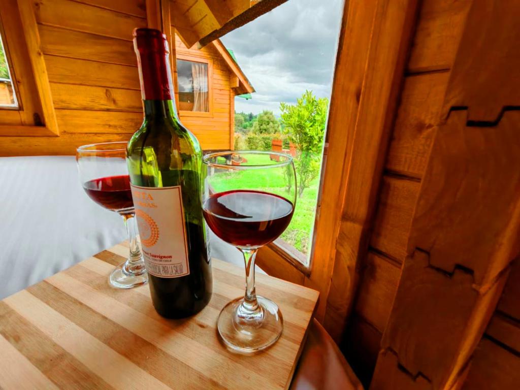 a bottle of wine and two glasses on a table at Tacama, acogedoras cabañas cerca a termales in Paipa
