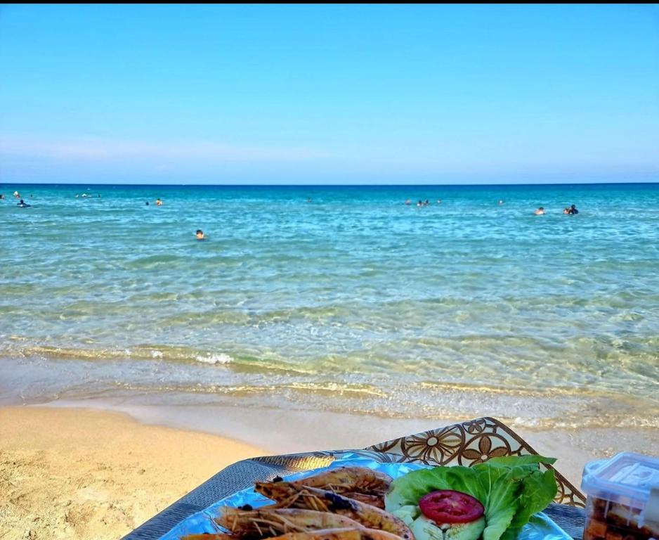 a plate of food on the beach with people in the ocean at Liliane Appartement in El Haouaria