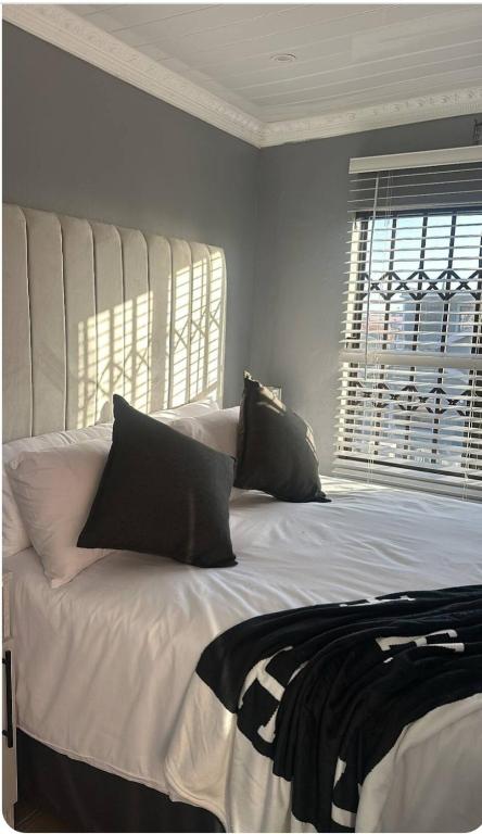 a white bed with black pillows and a window at Malithabo in Khayelitsha