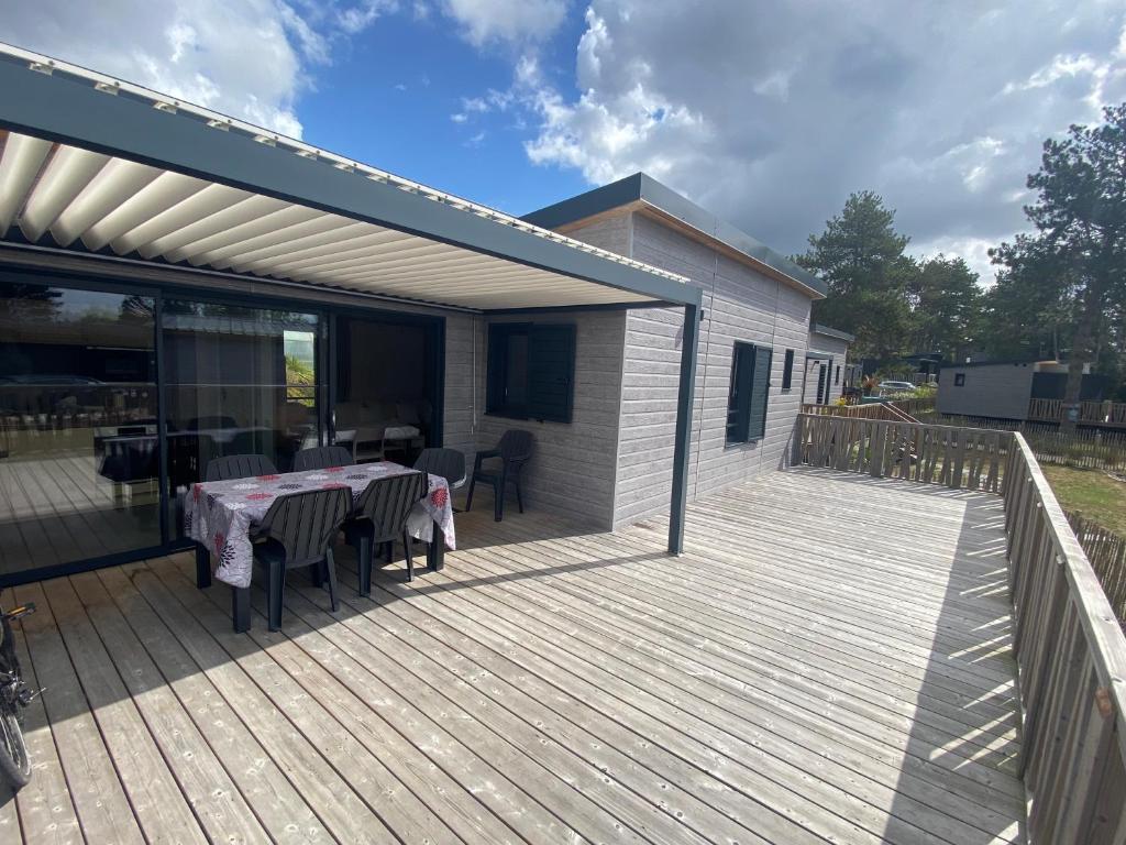 a wooden deck with a table and chairs on it at chalet de l'Edune 6 pers beau standing piscine couverte à 150m de la mer wifi inclus in Jullouville-les-Pins