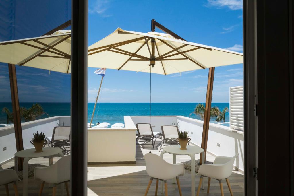 eine Terrasse mit weißen Stühlen, Tischen und Sonnenschirmen in der Unterkunft Hotel Miramare in Latina