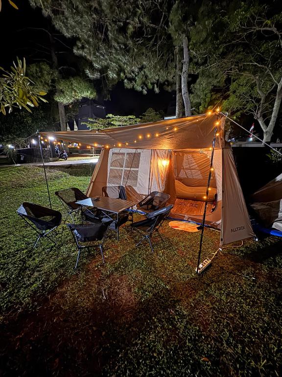 a tent with chairs and a table in the grass at night at Luxury Camp Waduk Darma in Haurkuning