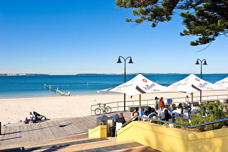 a beach with umbrellas and people sitting on the beach at Beach-Front Apartments in Sydney
