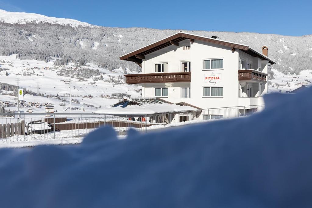 a building with snow on the ground in front of a mountain at Pitztal Living Apartments in Jerzens