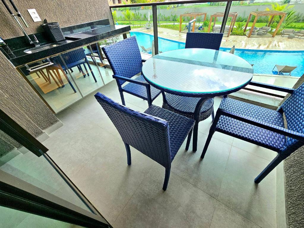a glass table and chairs with a pool in the background at Luxuoso e sofisticado Beach Class Summer by HM in Porto De Galinhas
