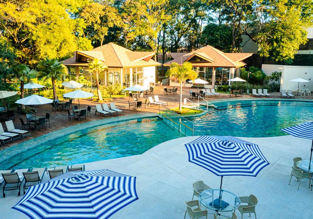 - une piscine avec des parasols, des tables et des chaises dans l'établissement Quarto em Resort de Foz do Iguaçu, à Foz do Iguaçu