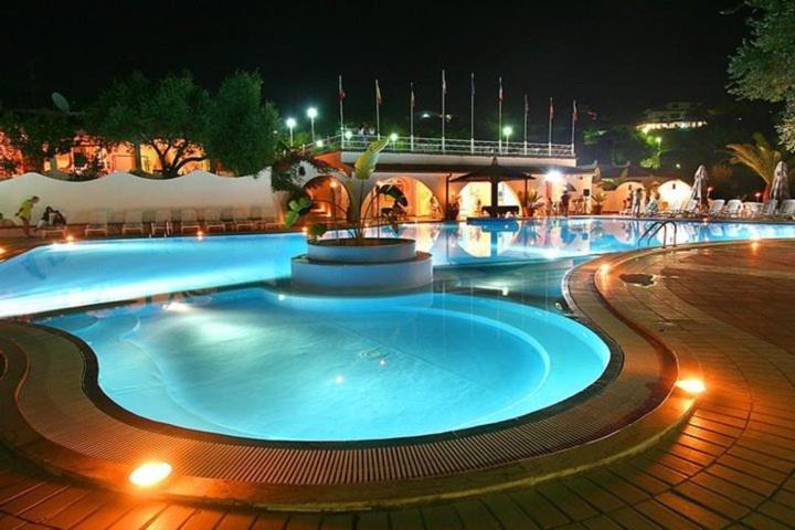 a large swimming pool with a fountain at night at Residence Villaggio Smedile in Capo Vaticano